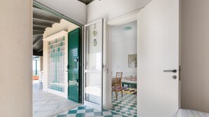 A room with a checkered floor, a bed, a chair, and a door leading to another room. - Attico La Baia (Gallipoli)