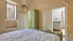 Un dormitorio con cama, un armario verde, una ventana y una puerta que da al baño.
