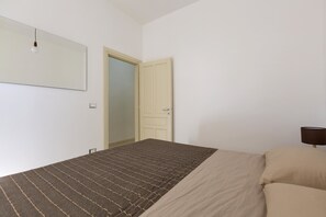 Quarto com cama, porta e luminária fixada na parede.