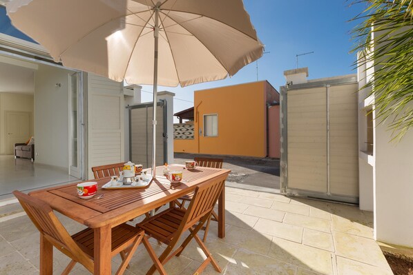 Mesa de madeira com cadeiras e um guarda-sol bege em um espaço de varanda.