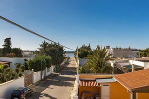 Uma rua residencial com casas, um carro estacionado e vista clara para o mar.