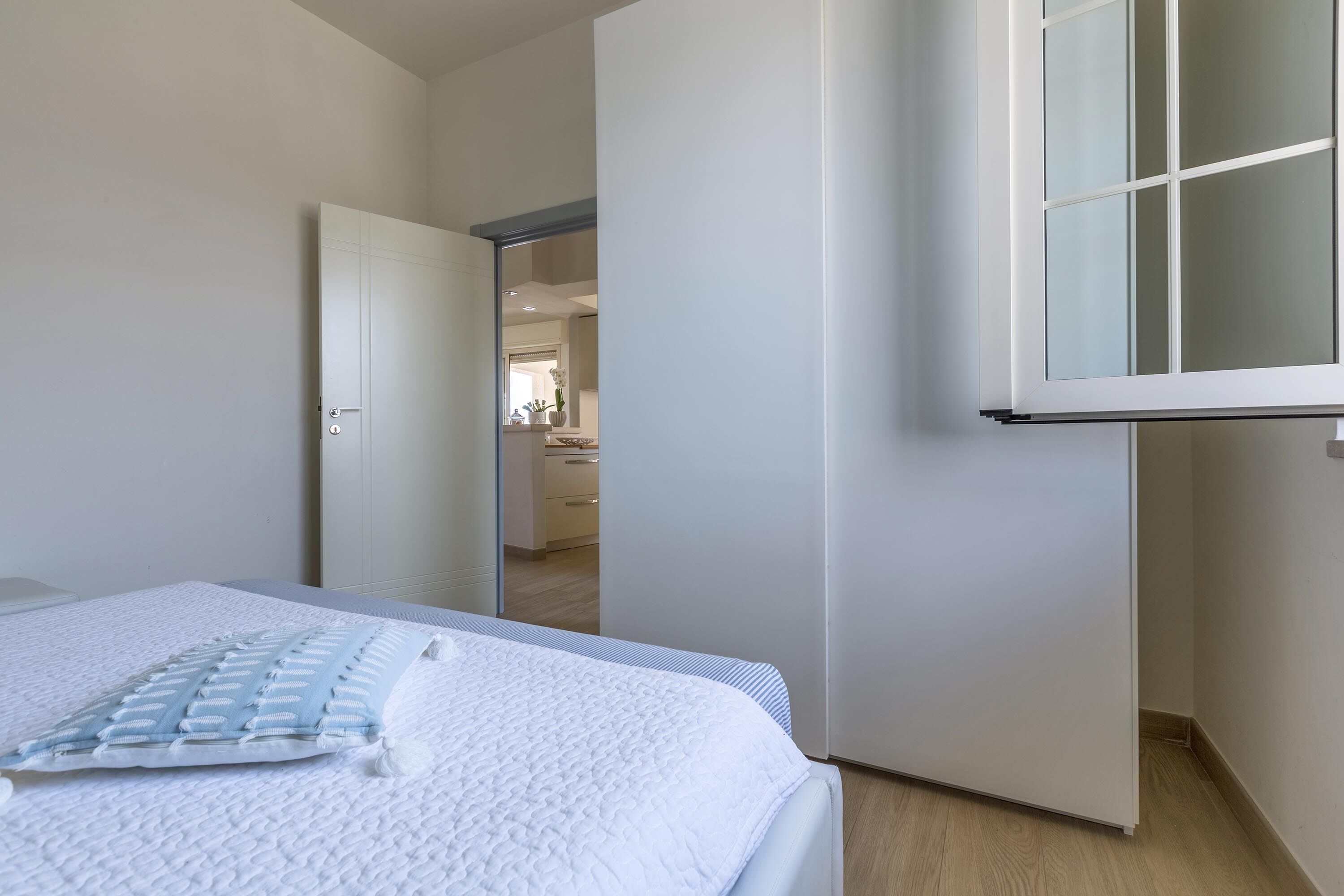 Un dormitorio con una cama, una puerta blanca y vistas a otra habitación.