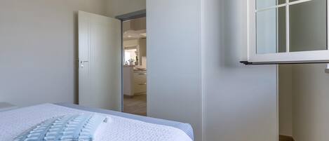 Un dormitorio con una cama, una puerta blanca y vistas a otra habitación.