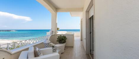 Un balcon avec vue sur la mer, des meubles blancs et une plante en pot.