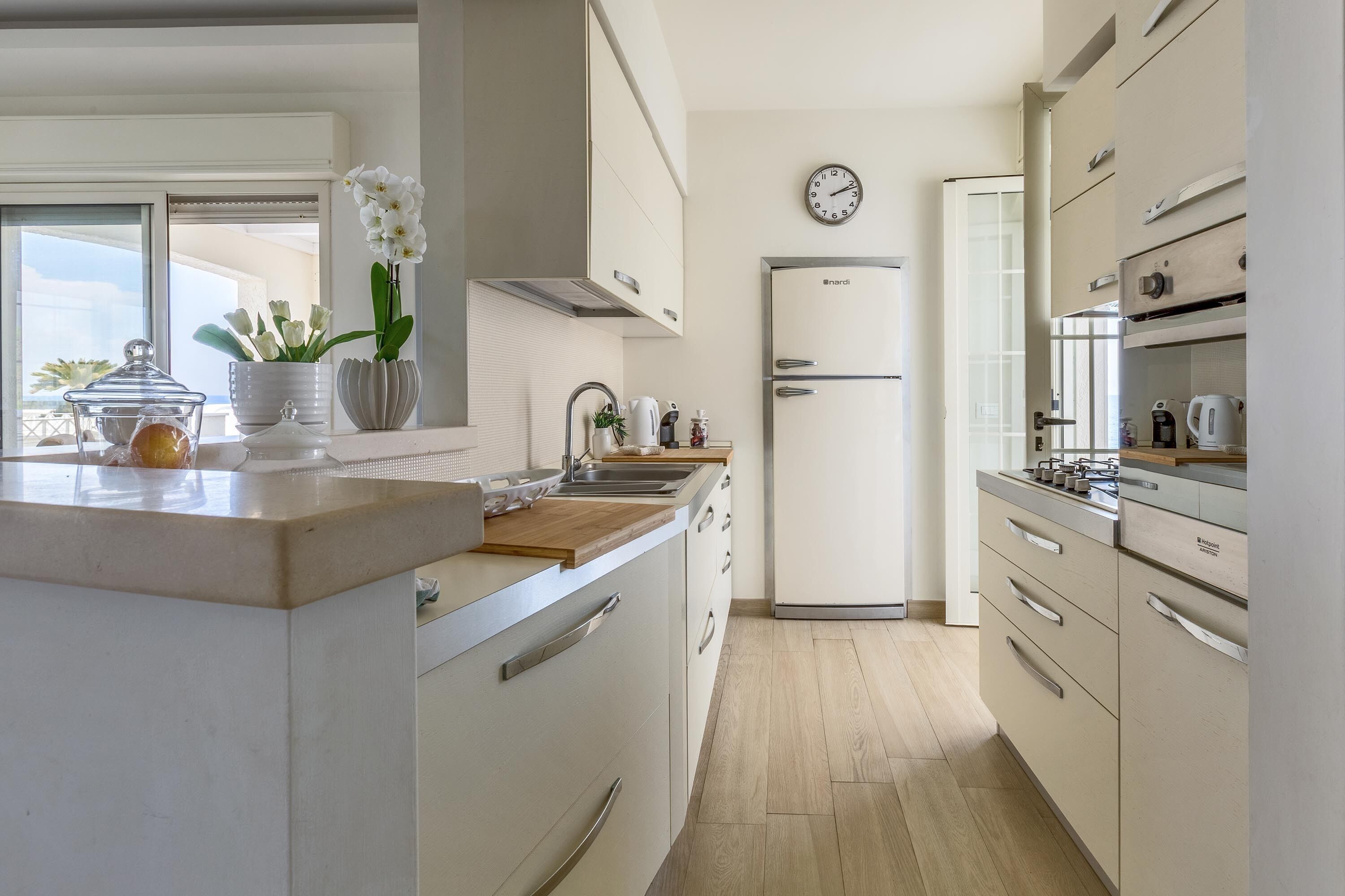Una cocina moderna con una isla grande, armarios blancos y un reloj en la pared.