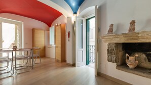 A spacious room with a wooden floor, a dining area with metal chairs, a fireplace with decorative items, and a door leading to an outdoor balcony. - La Casa di Clarissa (Otranto)