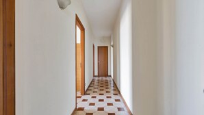 Un couloir avec un sol à motifs à carreaux, des portes en bois et des murs blancs.