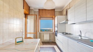 Une cuisine compacte avec vue sur la mer, un coin repas avec une nappe à motifs étoilés et des placards en bois.