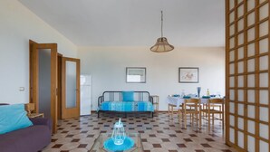 Un salon comprenant un canapé, une table basse, une table à manger avec des chaises, et donnant sur l’extérieur grâce à une porte.