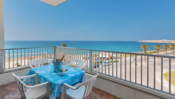 Un balcon avec une table dressée pour deux personnes, donnant sur une plage et la mer.