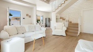 A spacious living area with a white sofa, a coffee table, and a staircase leading to an upper level. - Villa Adele (Maruggio)