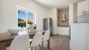 A modern kitchen with a stainless steel refrigerator, white cabinets, and a wooden dining table with white chairs. - Villa Adele (Maruggio)