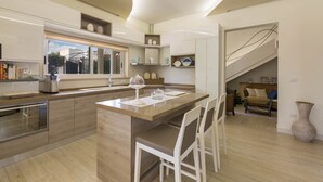 A modern kitchen with a central island, wooden cabinets, and a dining area with white chairs. - Villa Ariel (Porto Cesareo)