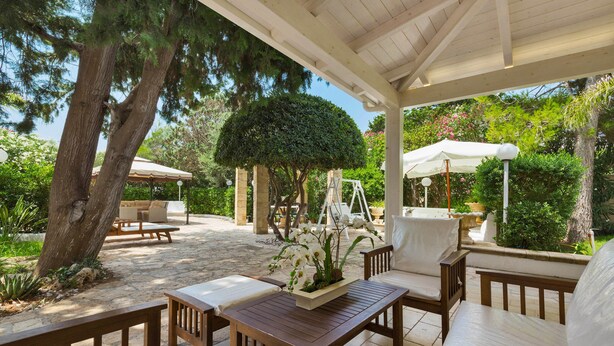 An outdoor patio with wooden furniture, a stone floor, and a pergola. - Villa Ariel (Porto Cesareo)