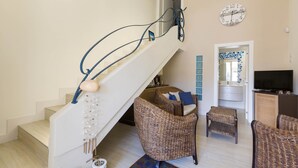 A staircase with blue handrails, wicker furniture, a clock, and a television in a living area. - Villa Ariel (Porto Cesareo)