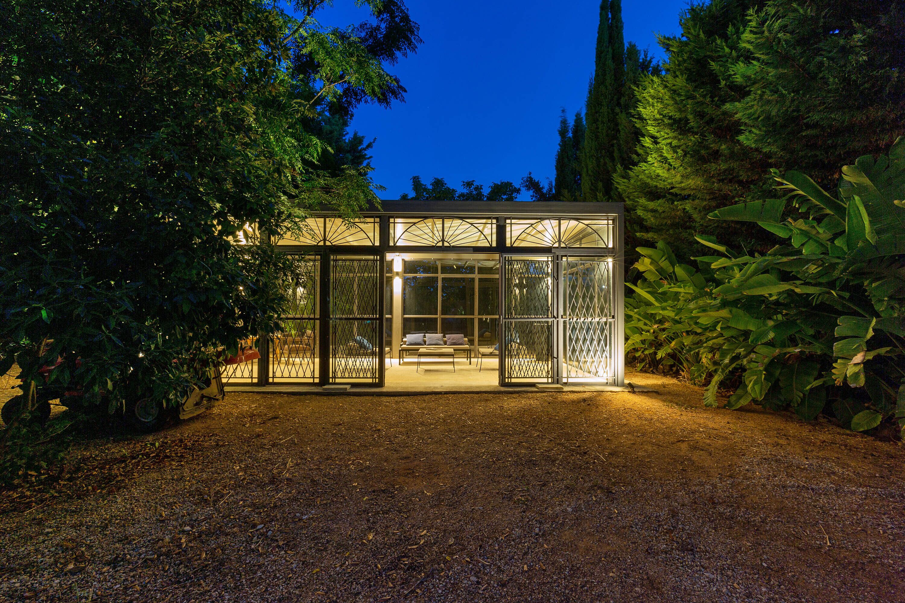 A glass-enclosed structure with a bench inside, surrounded by dense foliage.