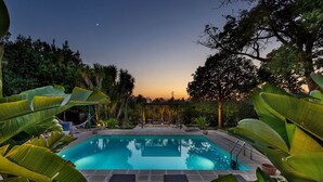 Une piscine entourée de plantes et d’arbres tropicaux, avec des chaises longues pour se détendre.