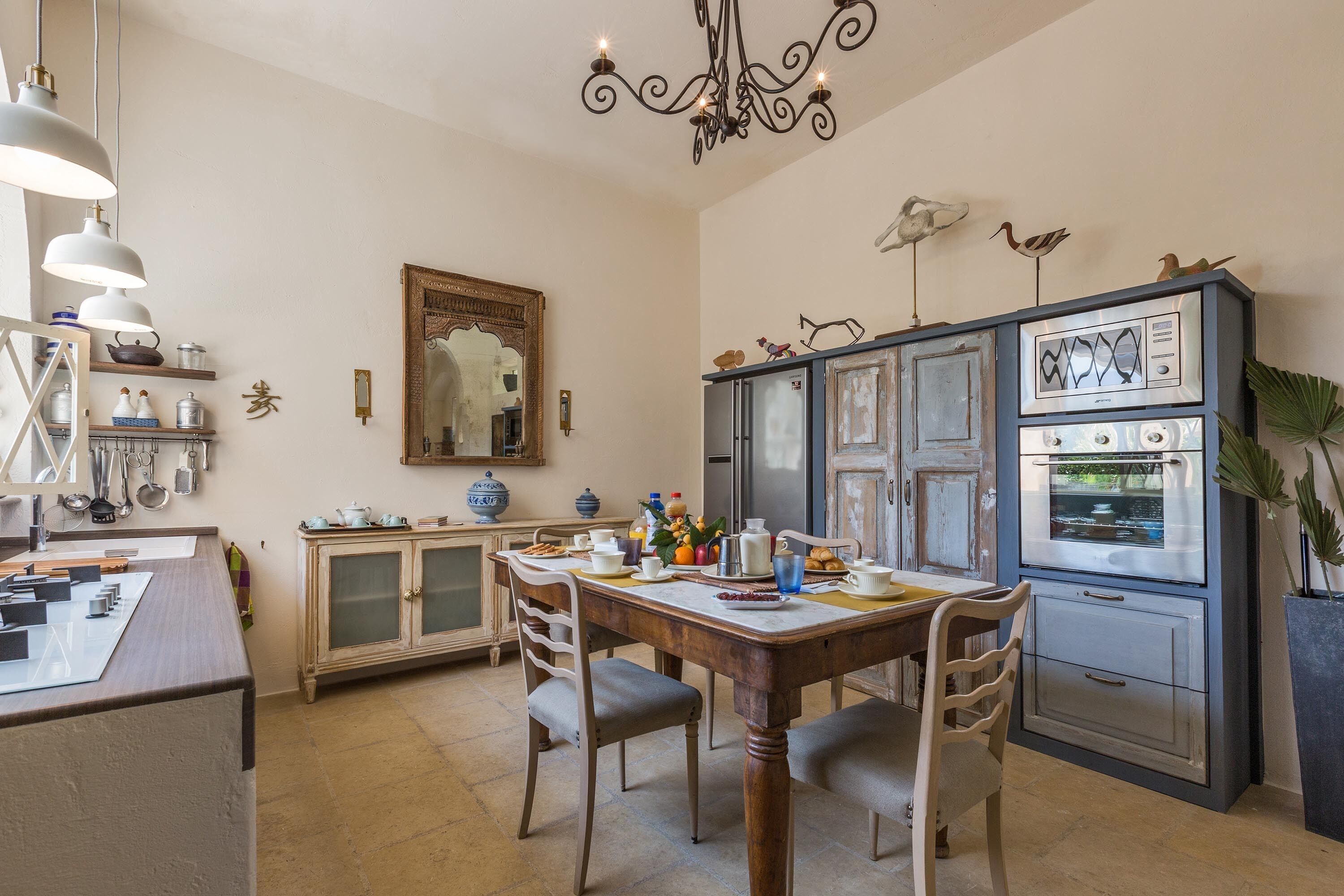 A kitchen with a wooden table, chairs, a chandelier, and a refrigerator.