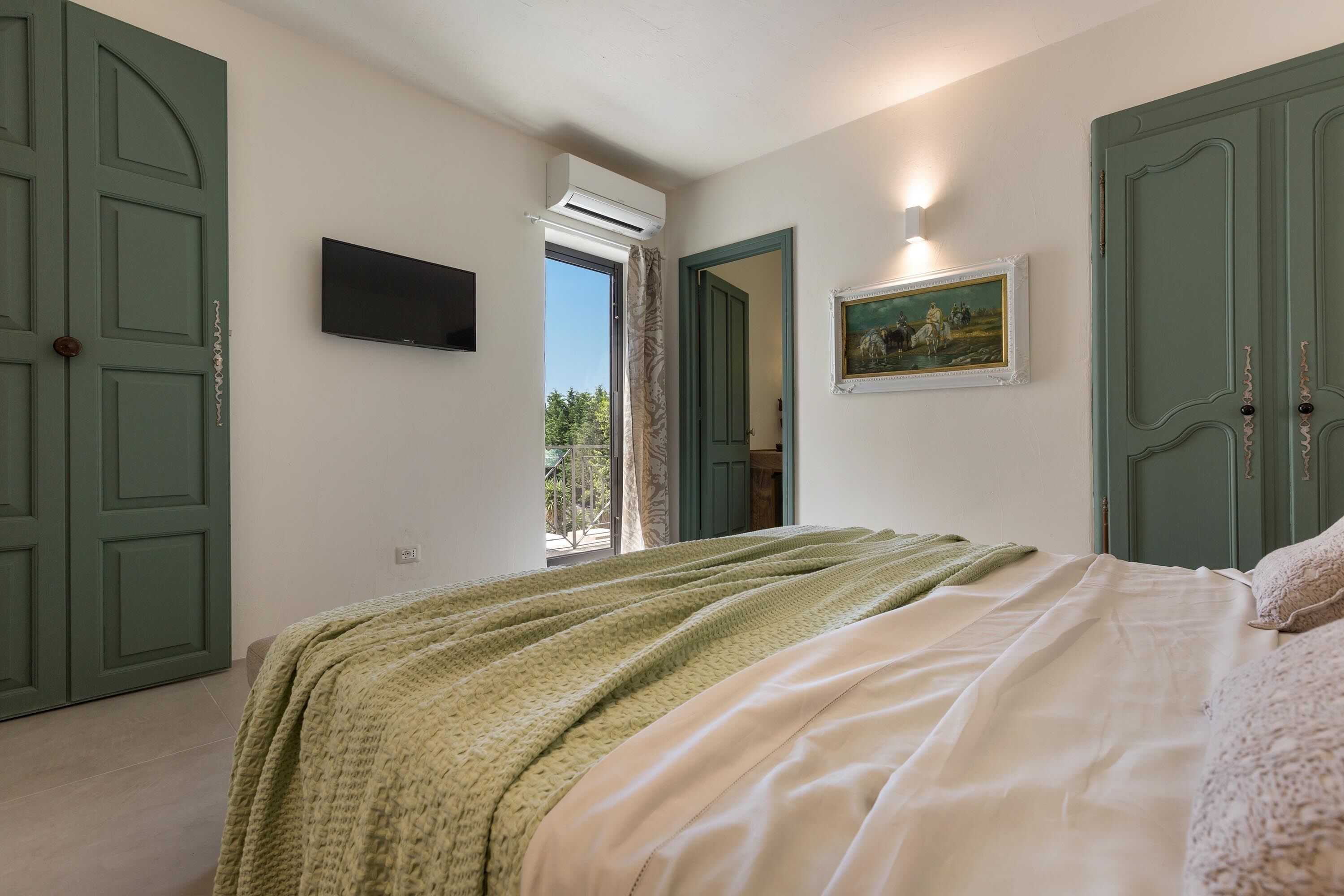 A bedroom with a bed, a television, and a painting on the wall.