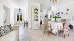 A spacious living area with a white sofa, a dining table with wicker chairs, a cabinet, and a chandelier. - Villa Chiara (Ruffano)