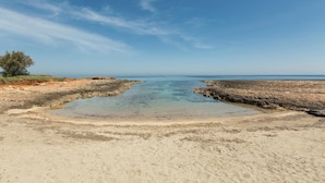 Una playa con agua cristalina, orilla de arena y zonas rocosas.