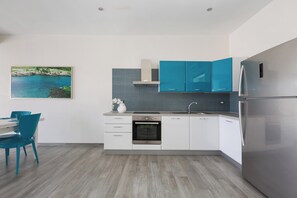 A modern kitchen with white cabinets, a stainless steel refrigerator, a built-in oven, and a blue chair.