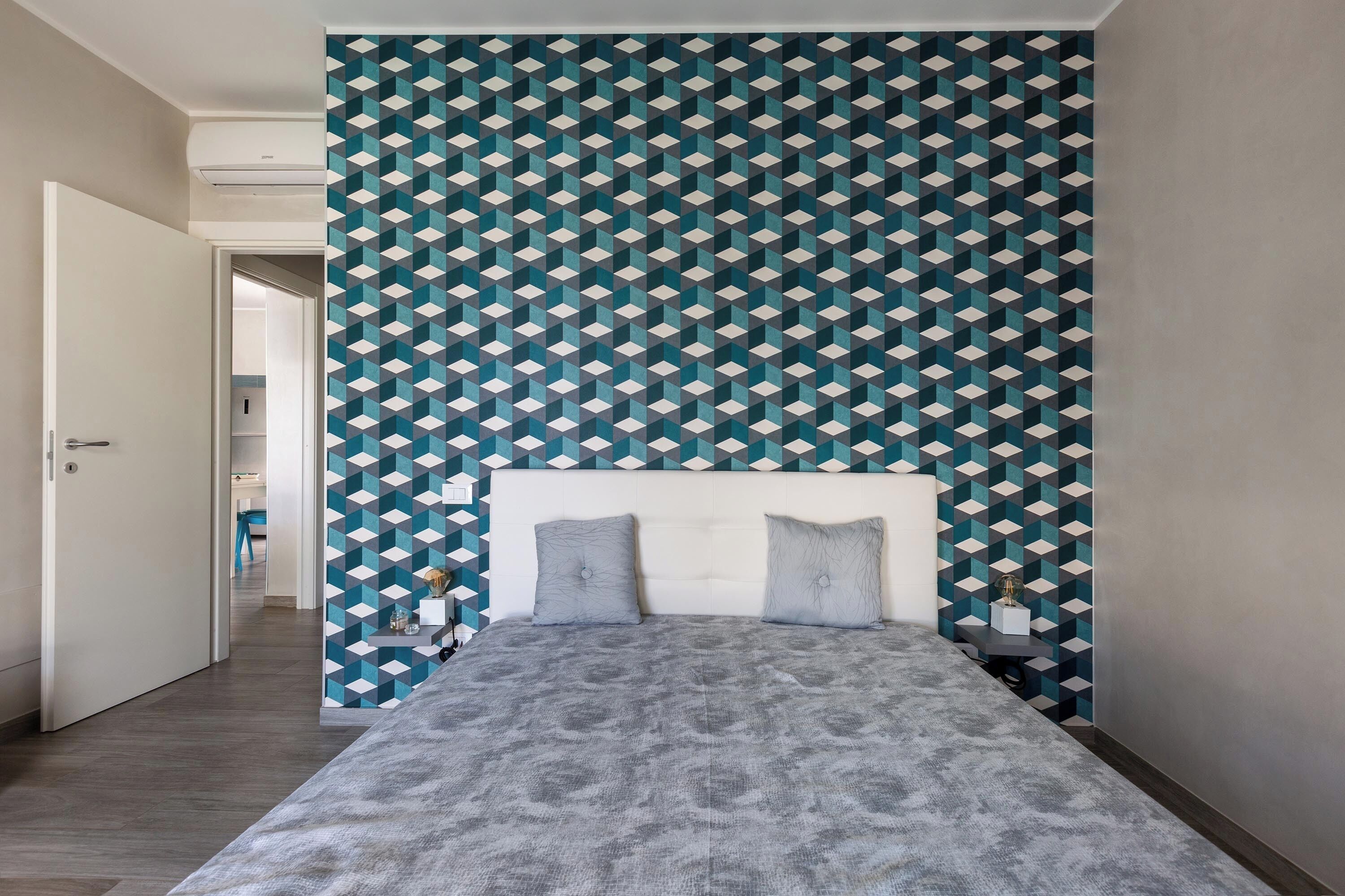 Ein Schlafzimmer mit einer Wand mit Muster, einem Bett mit grauer Bettwäsche und einem Nachttisch.
