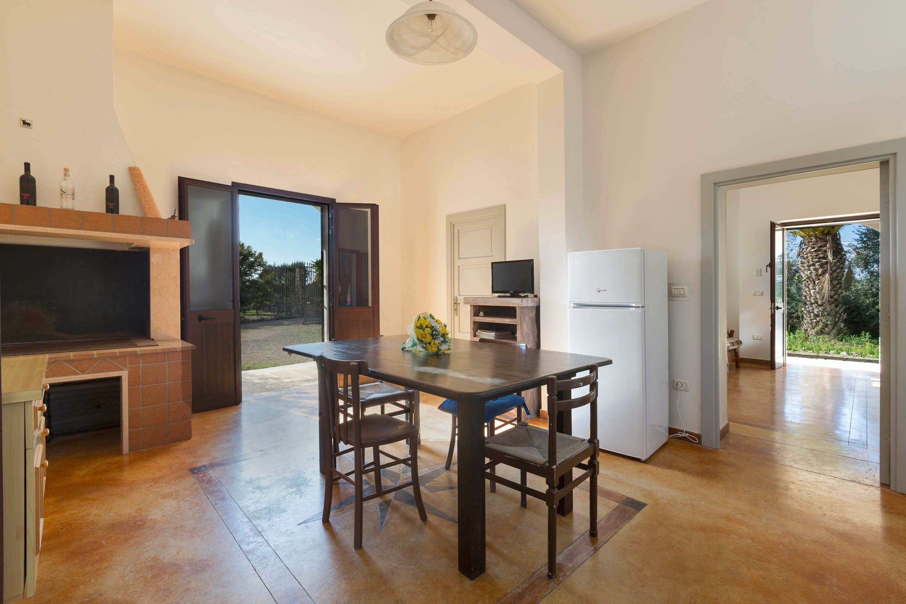 A spacious kitchen with a dining table, chairs, a TV, and a refrigerator.