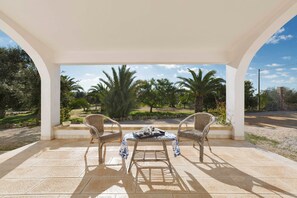 An outdoor patio with two wicker chairs and a small table, surrounded by a white pergola and palm trees. - Villa Giardino dello Ionio (Nardò)