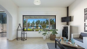 A modern living room with a large window, a flat-screen TV, a sofa, and a coffee table with a tray of glasses and a plate. - Villa Hoara (Brindisi)
