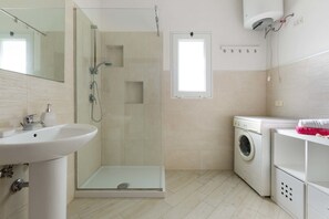 Un baño moderno con ducha de vidrio, lavamanos, lavadora y una ventana pequeña.