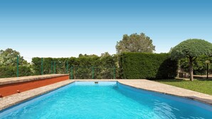 A rectangular swimming pool with a clear blue water surface, surrounded by a low brick wall and a green fence. - Villa Marù (Taurisano)