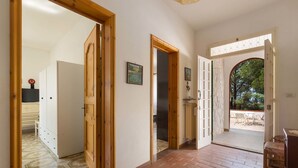 A hallway with wooden doors leading to different rooms, a tiled floor, and a view of an outdoor patio area. - Villa Marù (Taurisano)