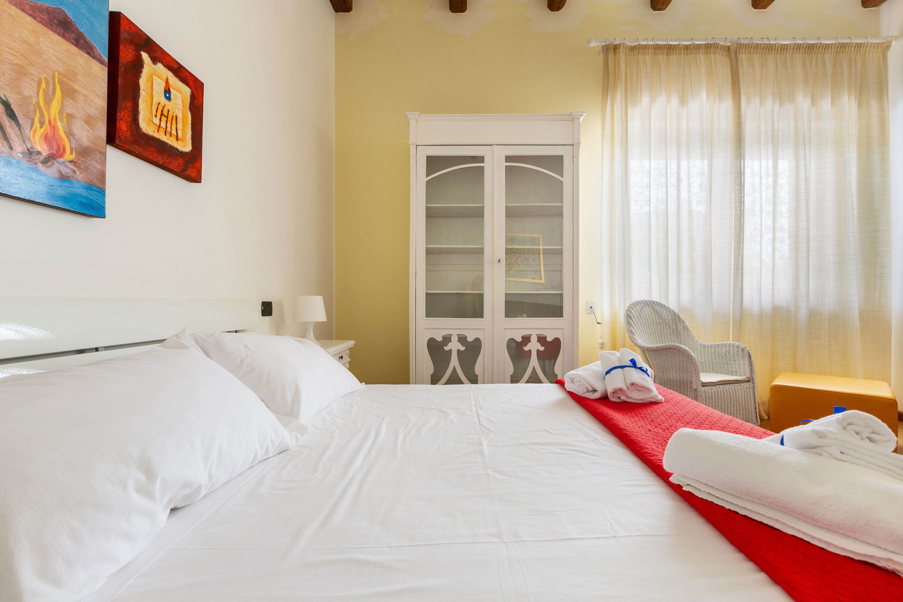 Habitación de hotel con una cama grande, un armario, una silla y una ventana con cortinas.