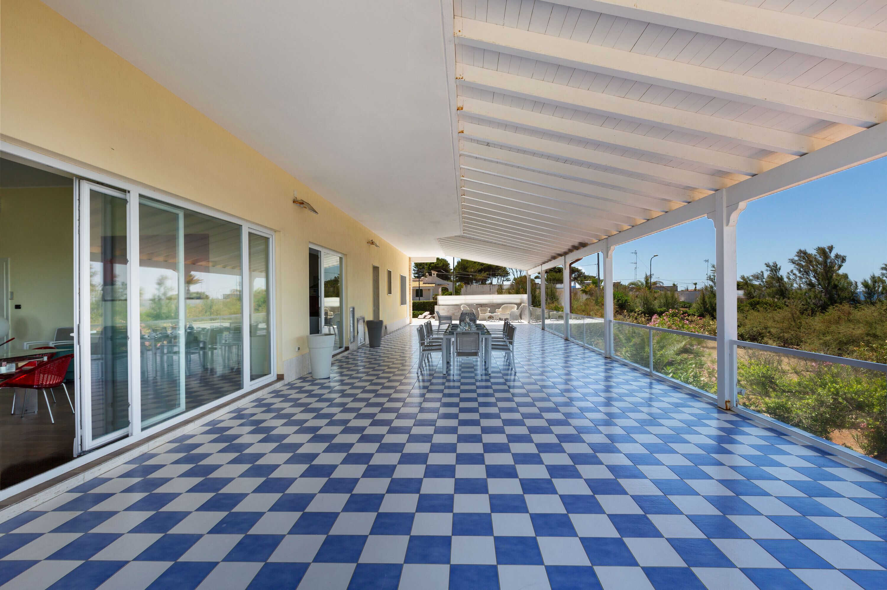 A covered outdoor area with a checkered floor, glass sliding doors, and a table with chairs.