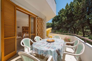A balcony with a table and chairs, a wooden door, and a view of trees.