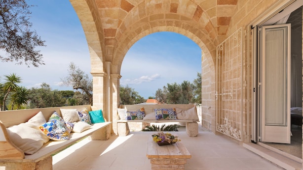An outdoor patio with stone benches and a wooden table, an archway, and a view of the surrounding landscape. - Villa Satis (Casarano)