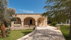 A stone building with three arches, a paved pathway, and surrounding greenery. - Villa Satis (Casarano)