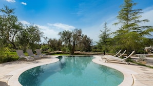A circular pool with lounge chairs around it, surrounded by trees and greenery. - Villa Satis (Casarano)