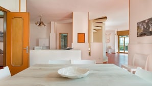 A modern dining area with a marble table, white chairs, and a wooden door. - Villa Scirocco (Porto Cesareo)