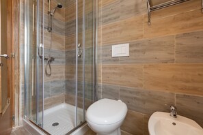 Une salle de bain avec une douche à parois de verre, des toilettes blanches et un lavabo sur colonne.