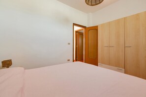 A bedroom with a bed, wooden wardrobe, and a wicker chair. - Villa Scirocco (Porto Cesareo)