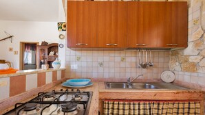 A kitchen with wooden cabinets, a gas stove, a sink, and a stone wall. - Villetta Baron Beach (Porto Cesareo)