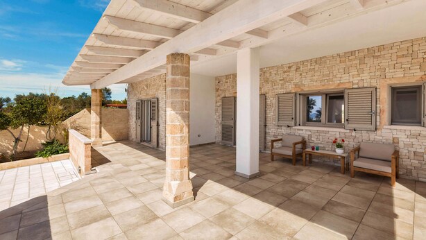 Un patio couvert doté de murs en pierre, d’une pergola et de mobilier d’extérieur.