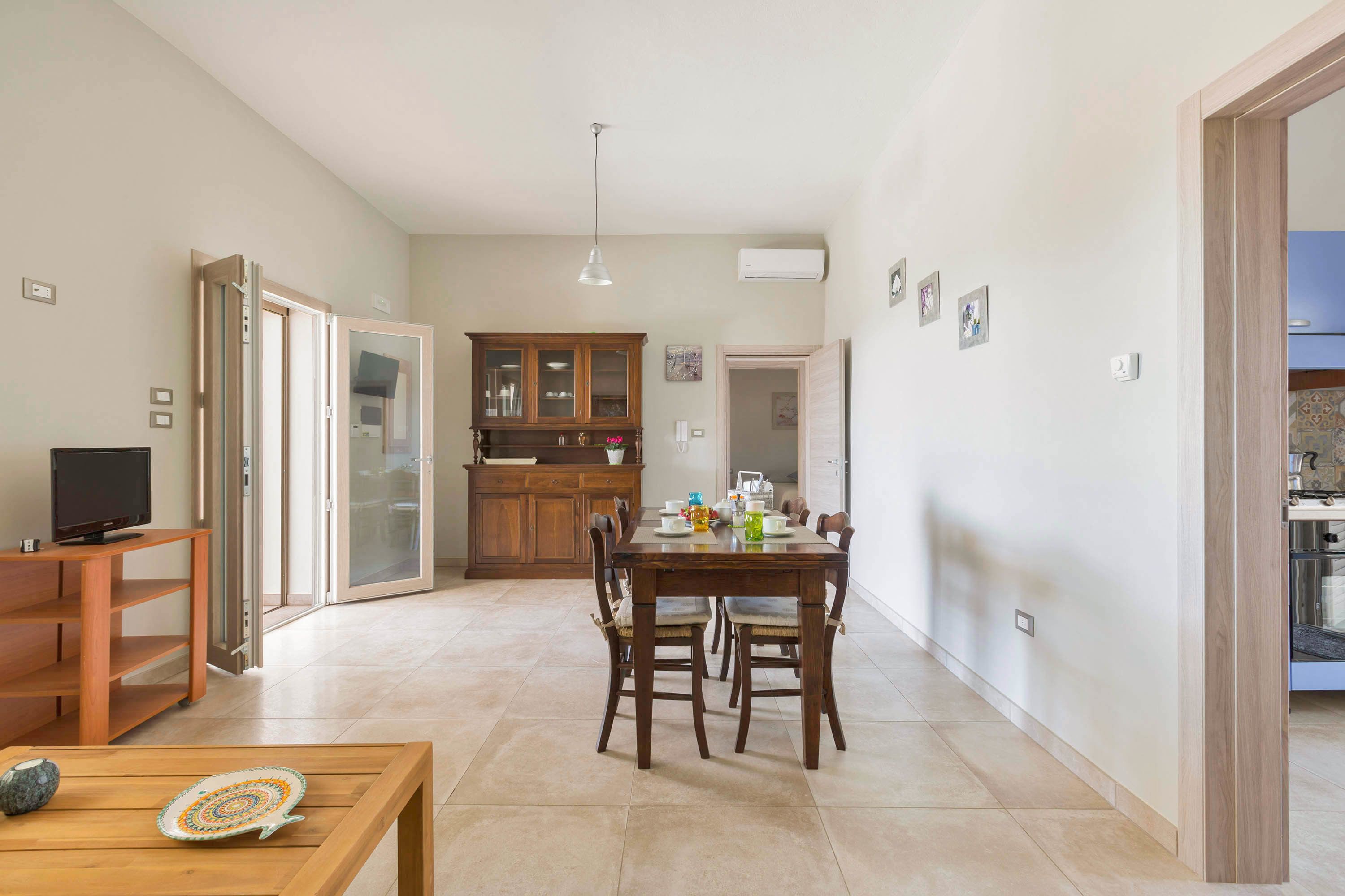 A spacious living area with a wooden dining table, chairs, and a TV on a stand.