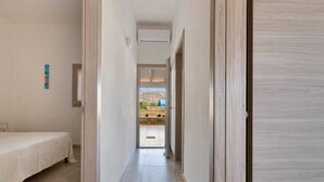 Un couloir étroit, avec un lit sur la gauche et une porte en bois sur la droite.