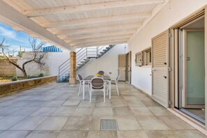 Un patio cubierto con una mesa y sillas, una escalera que sube a un nivel superior y un ventanal corredero.