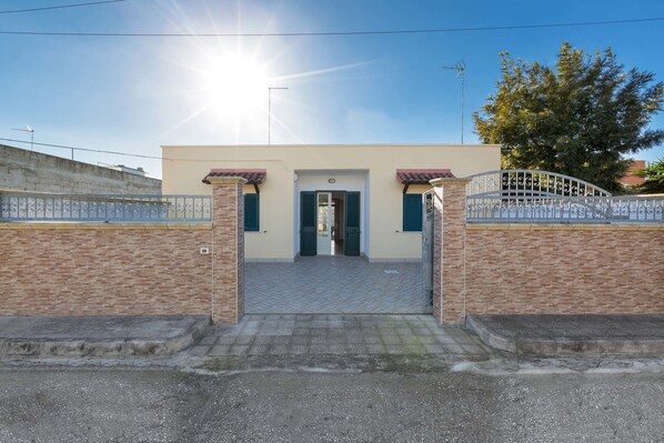 A building entrance with a gated driveway, a tiled pathway, and a clear sky.