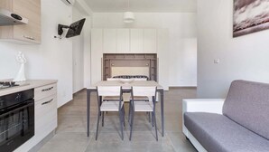 A modern kitchen with a dining table and chairs, a built-in oven, and a grey sofa.