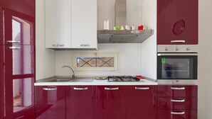 Une cuisine avec des meubles de couleur rouge, un plan de travail blanc, une cuisinière à gaz et un four.